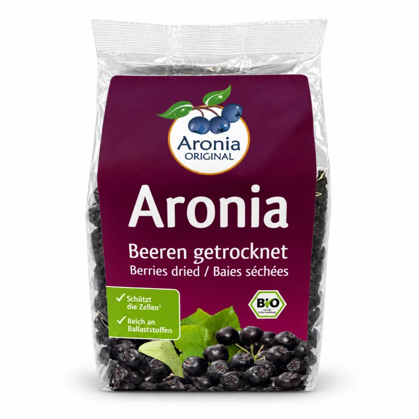 Pose med tørrede aroniabær, et glas yoghurt med bær ovenpå og løse bær foran.