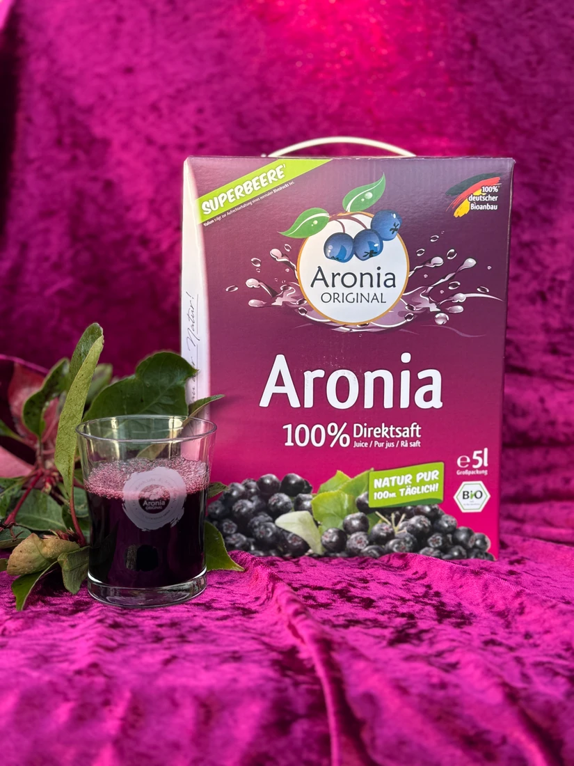 Bag-in-box med aroniasaft og et fyldt glas ved siden af.
