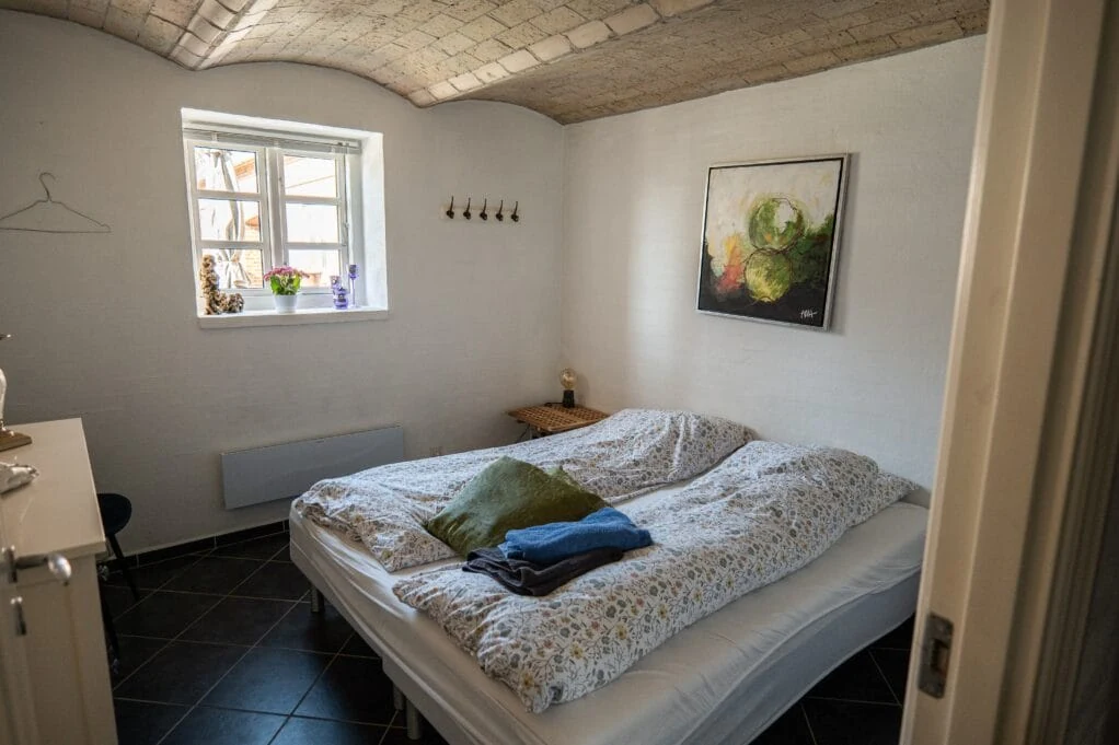 Dobbeltværelse med hvælvet loft, blomstret dyne og et lille vindue ud mod gården.